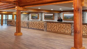 Eine geräumige Lobby mit Holzbalken, einem Steinkamin und Landschaftsbildern in Rahmen.