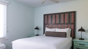 Un dormitorio con cama, dos mesitas de noche, ventilador de techo y ventana con persianas.