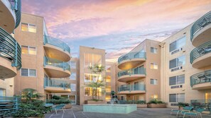 Un edificio de varios pisos con balcones, un patio central con una fuente y un cielo al atardecer.