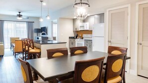 A modern kitchen with a central island, dining area with wooden chairs, and a ceiling fan. - Orlando 2BR Deluxe at Kingstown Reef – Pools, Near Disney & Universal (Orlando)