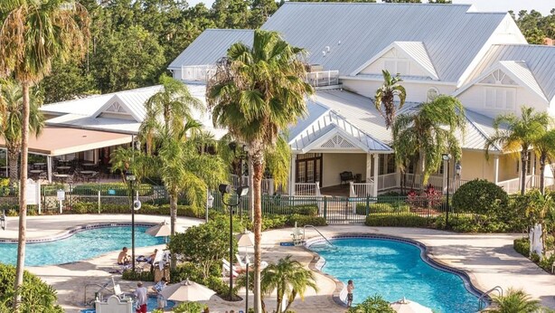 A resort with a swimming pool, palm trees, and a covered patio area. - Orlando 2BR Deluxe at Kingstown Reef – Pools, Near Disney & Universal (Orlando)