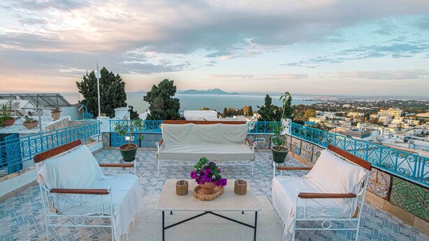 A terrace with a white sofa, two chairs, a table with a potted plant, and a view of the sea and cityscape. - Maison l'Étoile de Sidi Bou Saïd  S 09 (Sidi Bou Said)