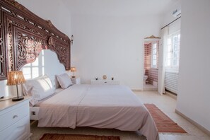 Ein Schlafzimmer mit einem großen Bett, einem Nachttisch mit Lampe, einer Kommode und einem durch eine offene Tür einsehbaren Badezimmer.