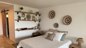 A bedroom with a large bed, wooden shelves with decorative items, and a small bedside table. - Cosy accommodation with sea view and swimming pool (Cul-de-Sac)