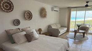 A hotel room with a bed, two chairs, a small table, and a view of the beach. - Cosy accommodation with sea view and swimming pool (Cul-de-Sac)