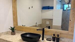 A bathroom with a stone countertop, a black basin, a wooden-framed mirror, and a towel rack. - Cosy accommodation with sea view and swimming pool (Cul-de-Sac)