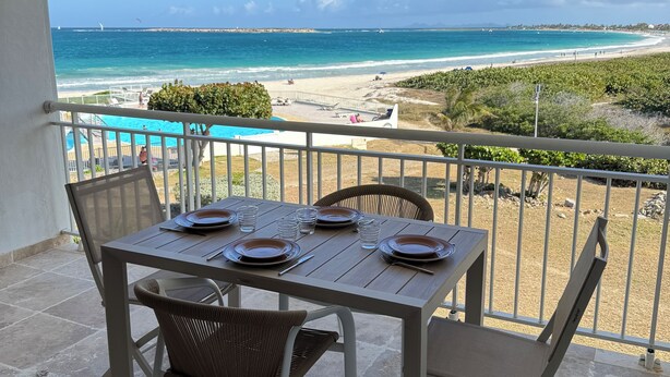 A balcony with a table set for dining, overlooking a beach with a clear view of the ocean and distant shoreline. - Cosy accommodation with sea view and swimming pool (Cul-de-Sac)