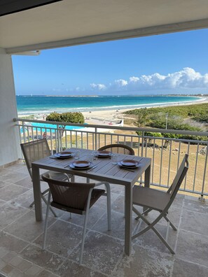 A balcony with a table set for dining, overlooking a beach with a clear view of the ocean and distant shoreline. - Cosy accommodation with sea view and swimming pool (Cul-de-Sac)