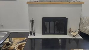 A modern living room with a flat-screen TV mounted above a fireplace, a black coffee table, and a patterned rug. - Cozy Compound Retreat Near Downtown & Highways (Detroit)