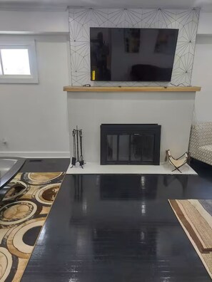 Un salon moderne avec un téléviseur à écran plat fixé au-dessus d’une cheminée, une table basse noire et un tapis à motifs.