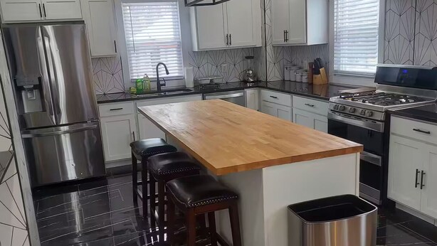 A modern kitchen with a central island, stainless steel appliances, and a black marble floor. - Cozy Compound Retreat Near Downtown & Highways (Detroit)