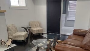 A modern living room with a brown leather sofa, two patterned armchairs, a glass coffee table, and a sliding door. - Cozy Compound Retreat Near Downtown & Highways (Detroit)
