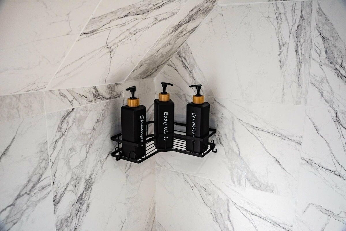 Une salle de bain avec un mur en marbre et trois distributeurs noirs portant l’étiquette « Bioderma ».