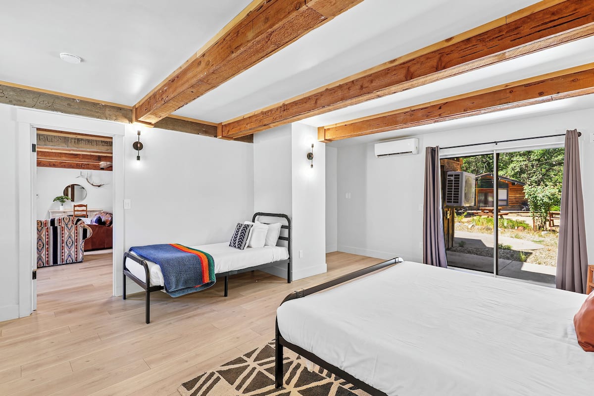 A bedroom with a large bed, a smaller bed, and a sofa bed. There is a wooden ceiling and a window with curtains.