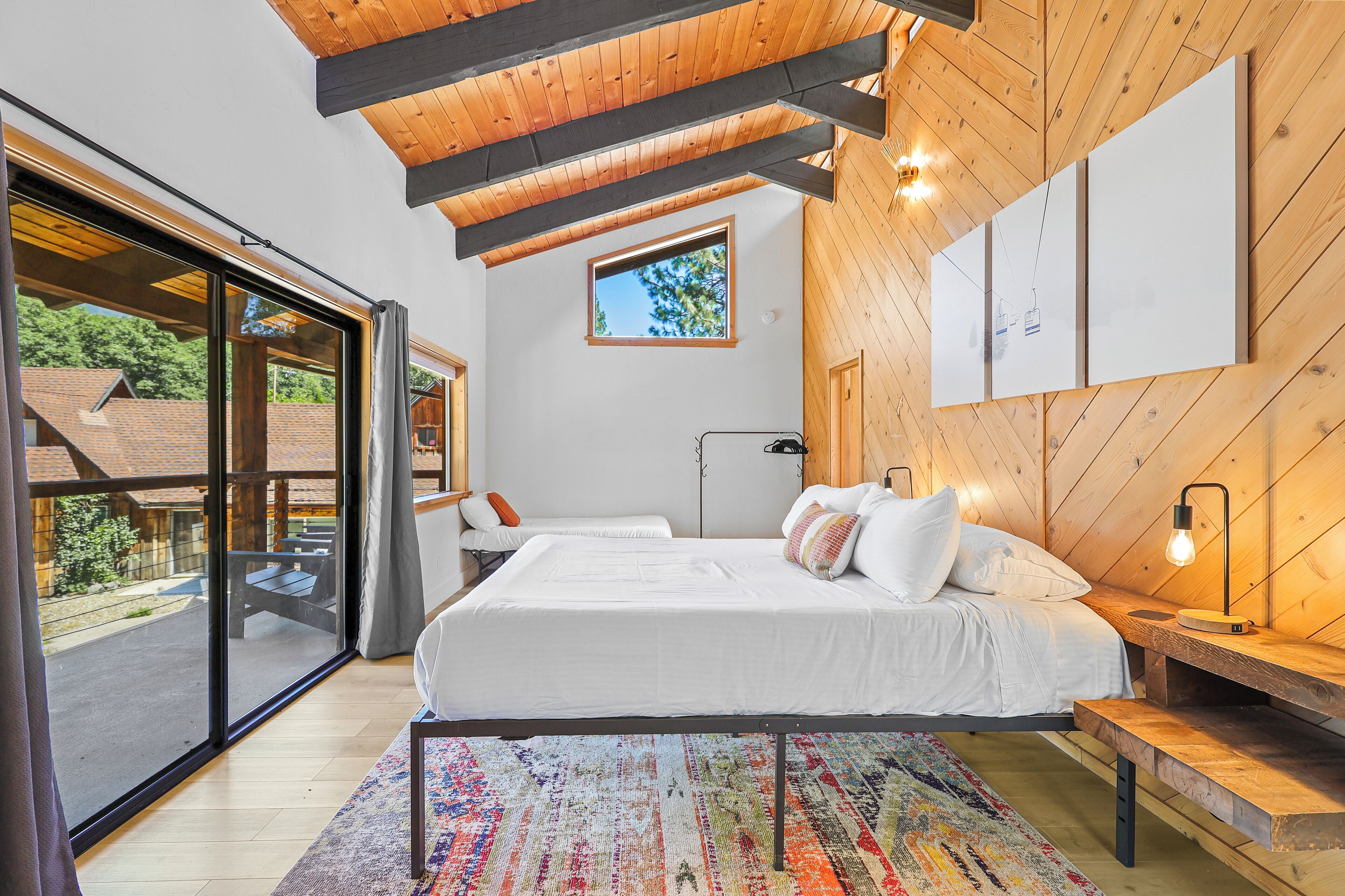 A bedroom with a large bed, a bench, a desk, and a view of the outdoors.