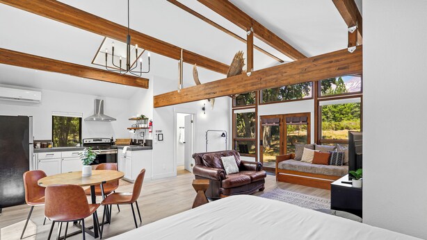 A spacious living area with a large bed, a dining table with chairs, a leather sofa, and a kitchen in the background. - Basecamp Lodge (Mount Shasta)