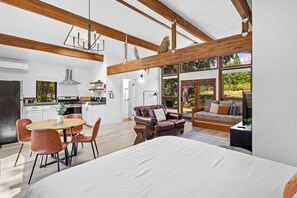 A spacious living area with a large bed, a dining table with chairs, a leather sofa, and a kitchen in the background. - Basecamp Lodge (Mount Shasta)