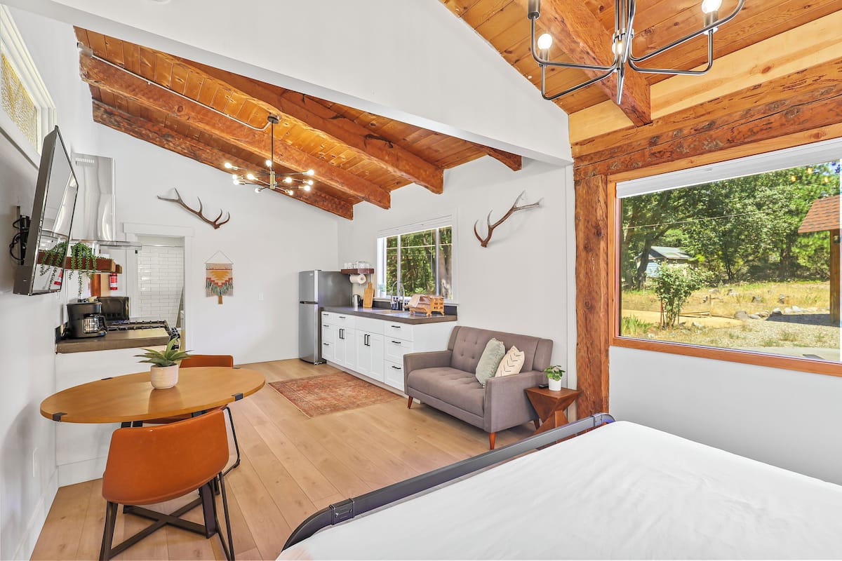 A modern kitchen with white cabinets, a wooden ceiling, and a large window overlooking a garden.