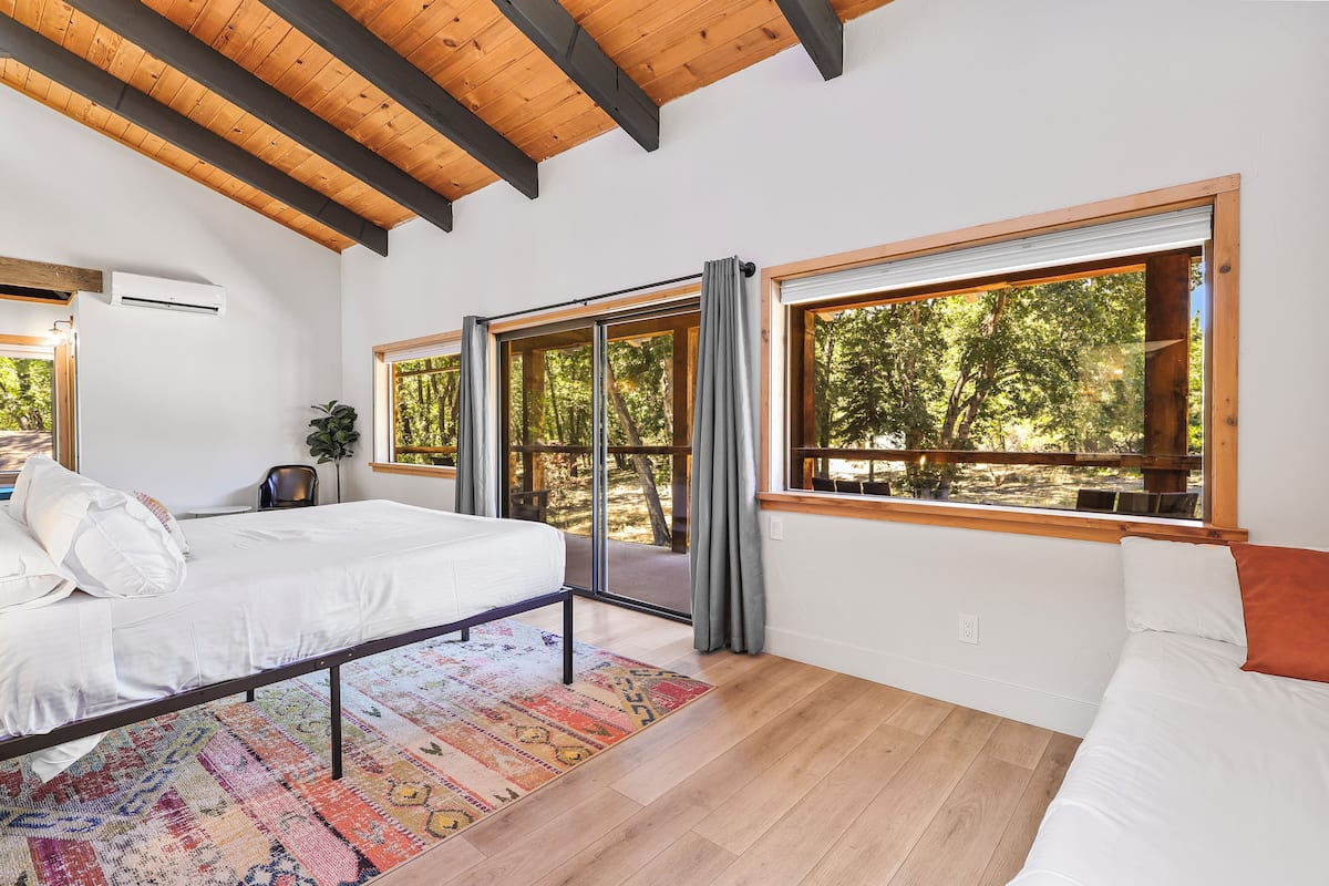 A bedroom with a bed, a large window, and a view of trees.