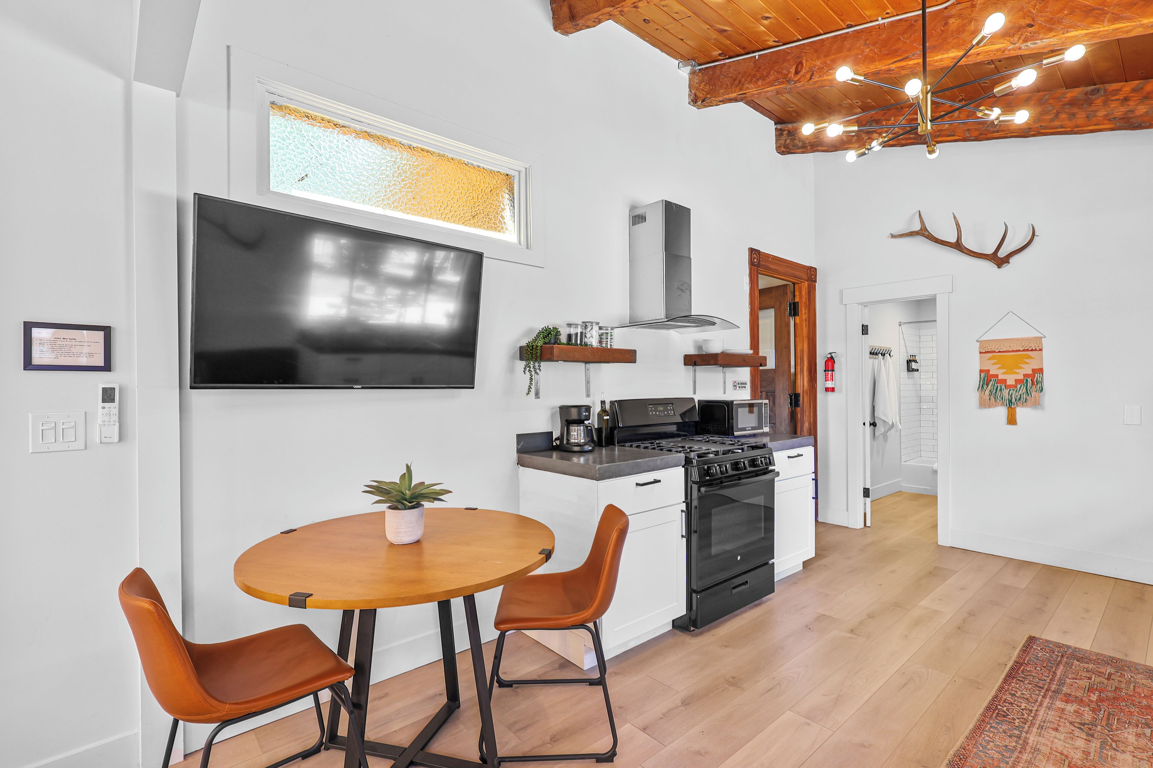 Una cocina moderna con un horno grande, microondas y un televisor de pantalla plana. Hay una zona de comedor con una mesa de madera y dos sillas.
