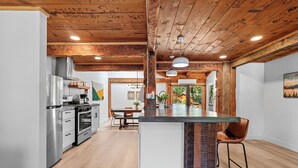 A modern kitchen with stainless steel appliances, a wooden ceiling, and a central island with bar stools. - Basecamp Lodge (Mount Shasta)
