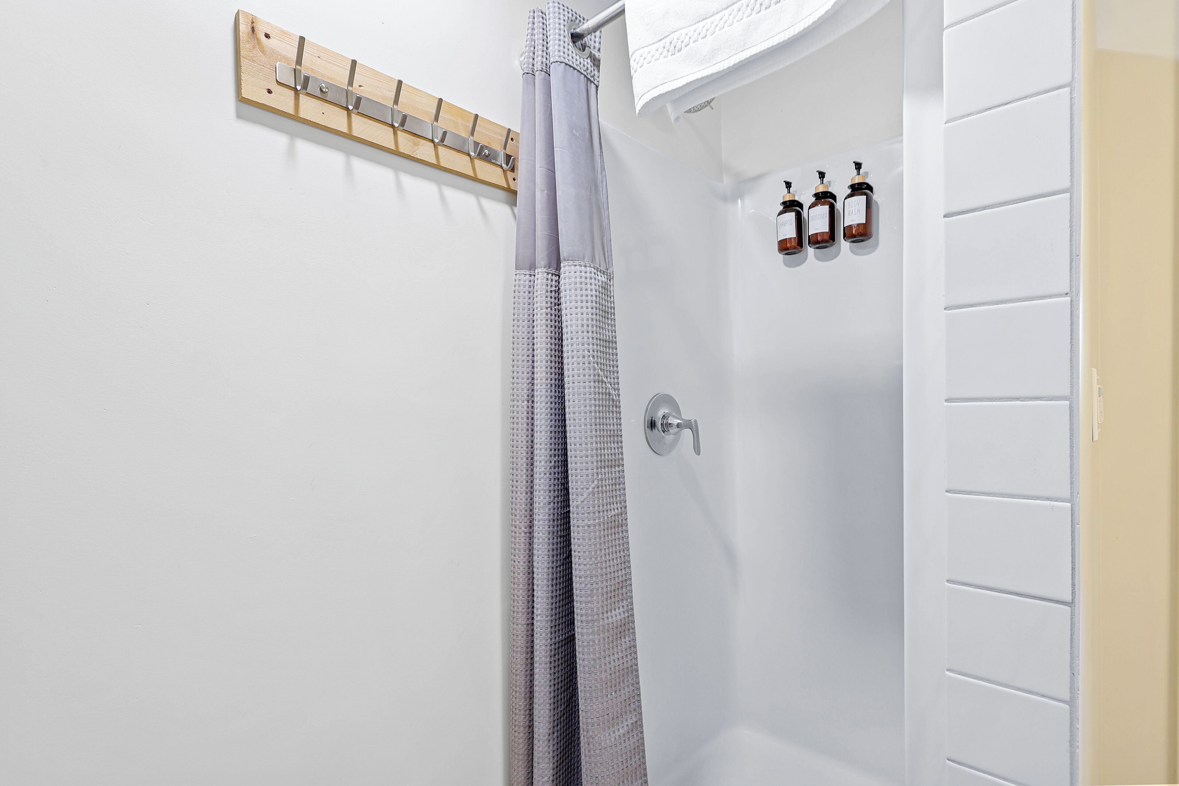 A bathroom with a shower curtain, a wooden towel rack, and three bottles of toiletries on the wall.