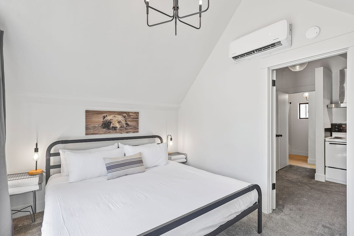 A bedroom with a bed, bedside table, lamp, and a painting on the wall.