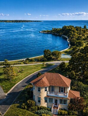 A two-story house with a wrap-around porch, a curved driveway, and a view of a large body of water. - Classic Coastal Family Home | Walk to Sea;King Bed (Gloucester)