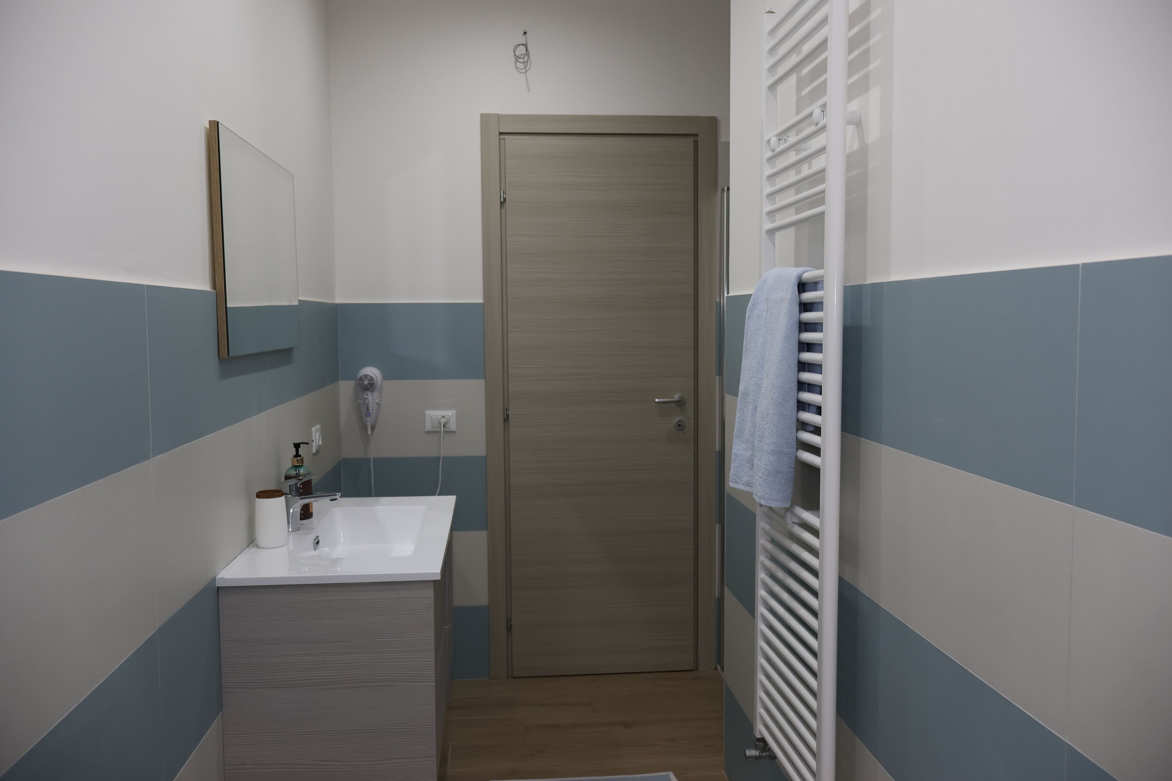 Ein Badezimmer mit Waschbecken, Spiegel, Handtuchhalter und einer Tür.