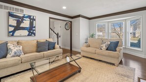 A living room with two beige sofas, a glass coffee table, and a large abstract painting on the wall. - A Home away from home - family friendly, central (Kansas City)