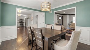 A dining area with a wooden table and chairs, a chandelier, and a view into the kitchen. - A Home away from home - family friendly, central (Kansas City)