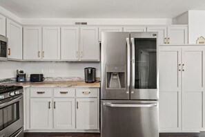 Una cucina moderna con mobili bianchi, elettrodomestici in acciaio inossidabile e un piano di lavoro in marmo.