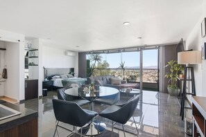 A modern living area with a dining table, chairs, a sofa, and a large window with a view.