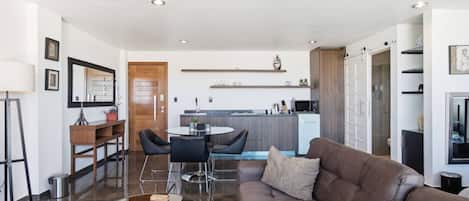 A modern living room with a brown leather sofa, a glass coffee table, and a dining area with a round table and chairs.