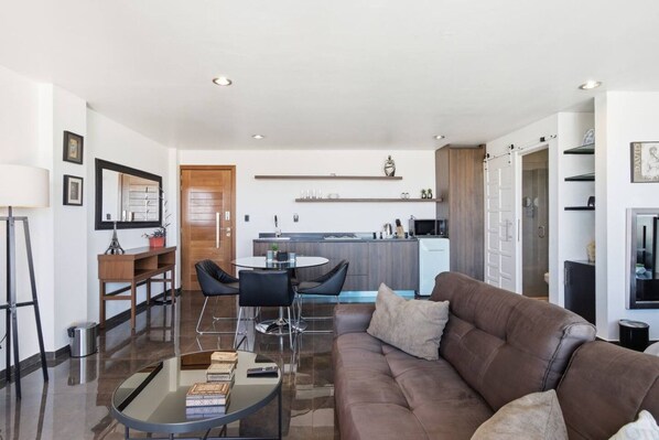 A modern living room with a brown leather sofa, a glass coffee table, and a dining area with a round table and chairs.