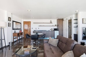 A modern living room with a brown leather sofa, a glass coffee table, and a dining area with a white table and black chairs.
