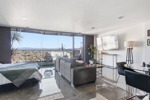 A modern hotel room with a balcony, a sofa, a bed, a TV, and a dining area.