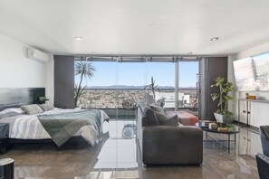 A modern hotel room with a large bed, a sofa, a small table, and a view of the city.