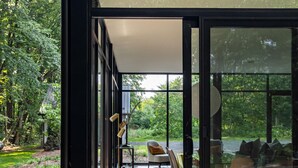 Ein modernes Haus mit großen Glasüren, die auf eine Terrasse mit Essgruppe und Gartenblick führen.