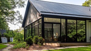 Ein modernes Haus mit einem großzügigen Wintergarten, umgeben von einem gepflegten Garten und einem Metalldach.