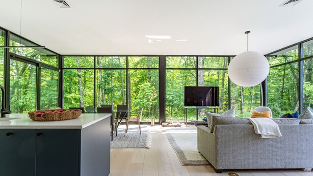 Ein modernes Interieur mit Küche, Essbereich und Wohnzimmer, ausgestattet mit großen Fenstern und einem Fernseher.