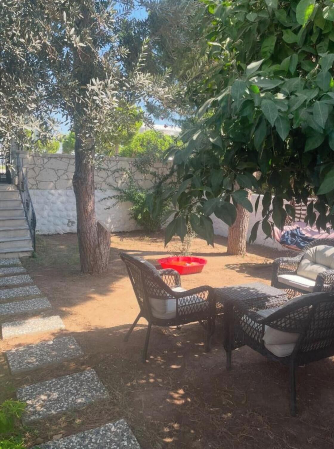 An outdoor patio area with wicker furniture, a stone wall, and a tree providing shade.