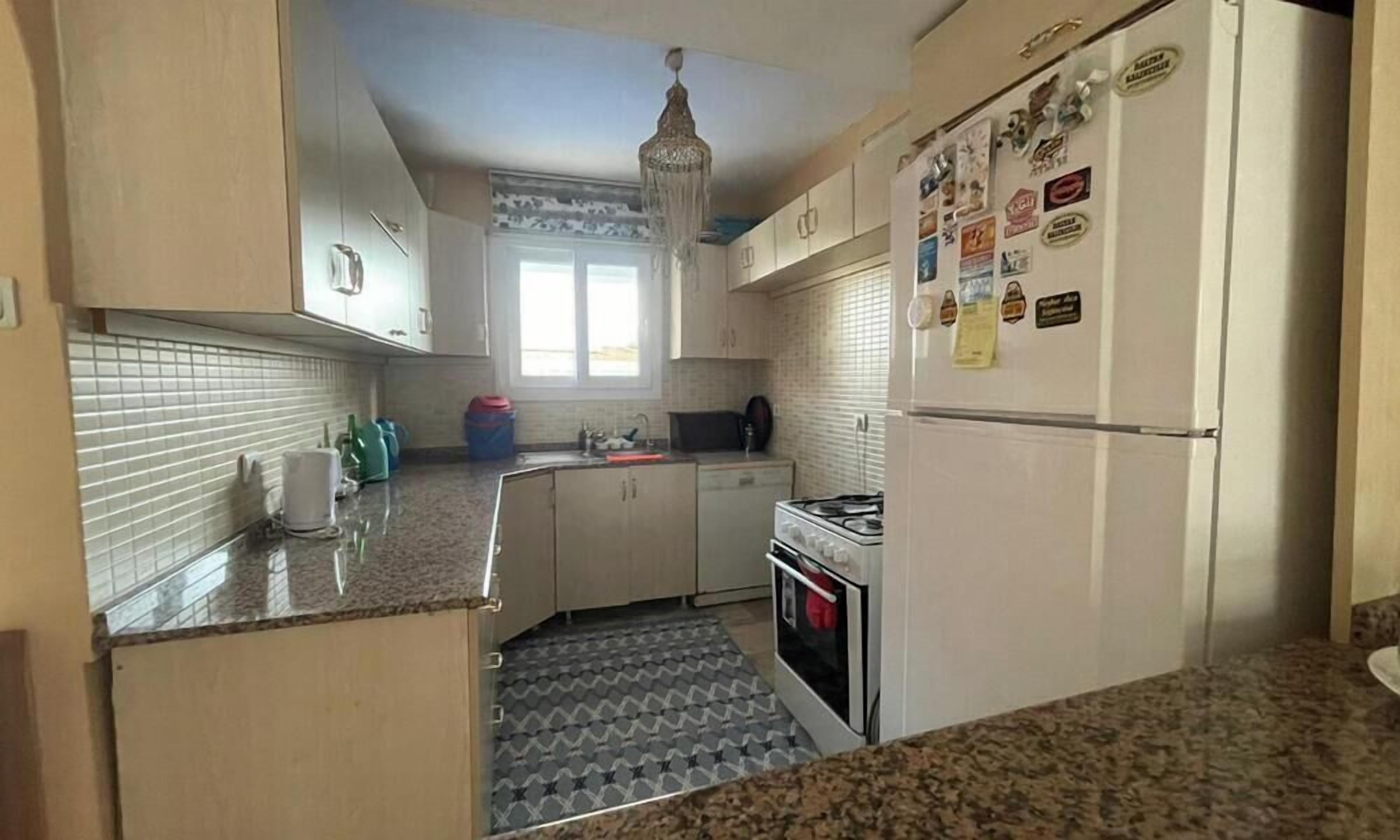 Una cocina con gabinetes blancos, encimera de granito, estufa a gas y refrigerador con imanes.
