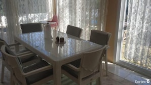 A dining area with a glass table surrounded by wicker chairs, a small decorative item on the table, and sheer curtains in the background.