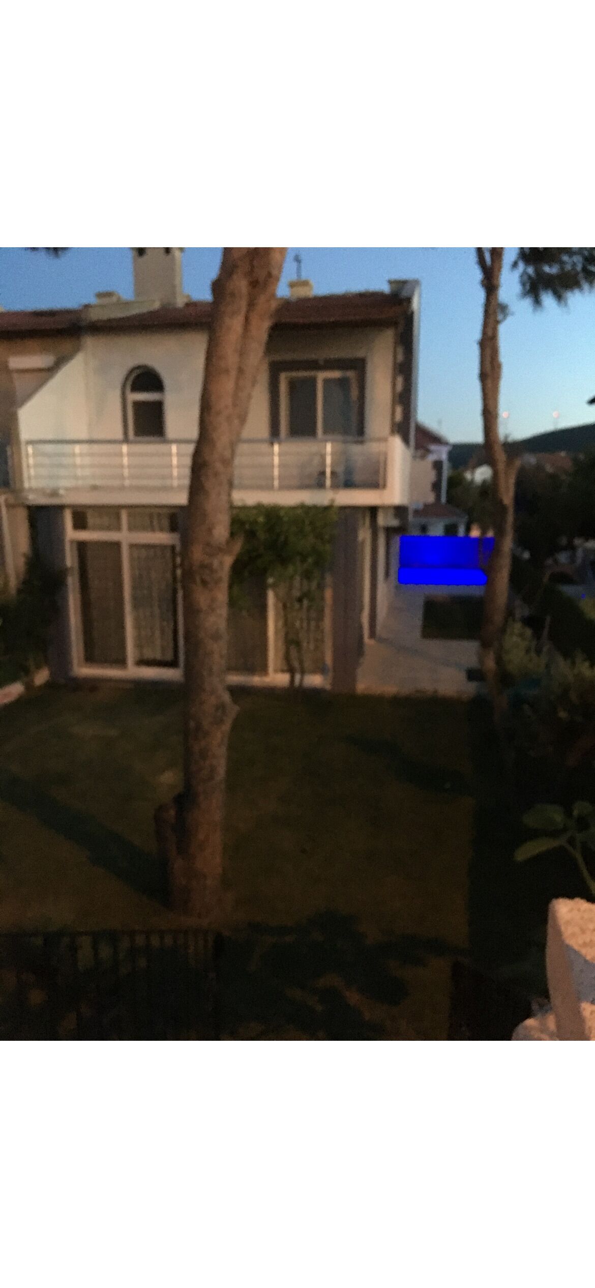 A modern two-story house with a balcony, a well-maintained lawn, and a tree in the foreground.