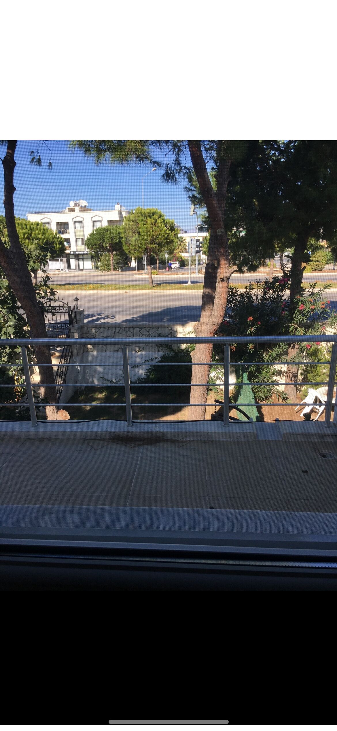 Vista desde una ventana sobre una calle con árboles, un edificio y una cerca.