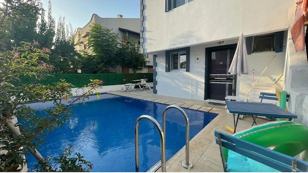 A swimming pool with a metal ladder, a sun lounger, and a small table.