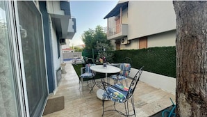 A patio area with a table and chairs, a tree, and a building in the background.