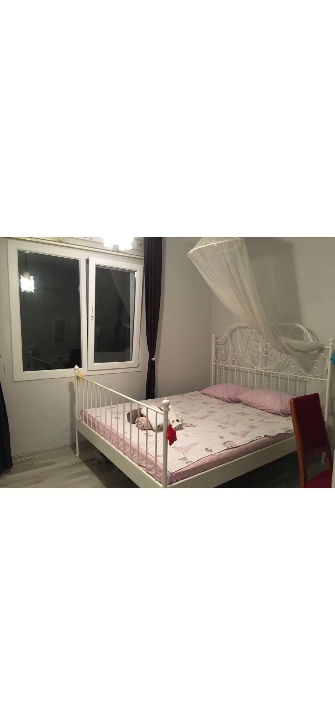 A single bed with a canopy, a window with curtains, and a chair.