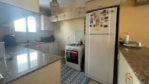A kitchen with granite countertops, a refrigerator with magnets, a stove, and a chandelier.